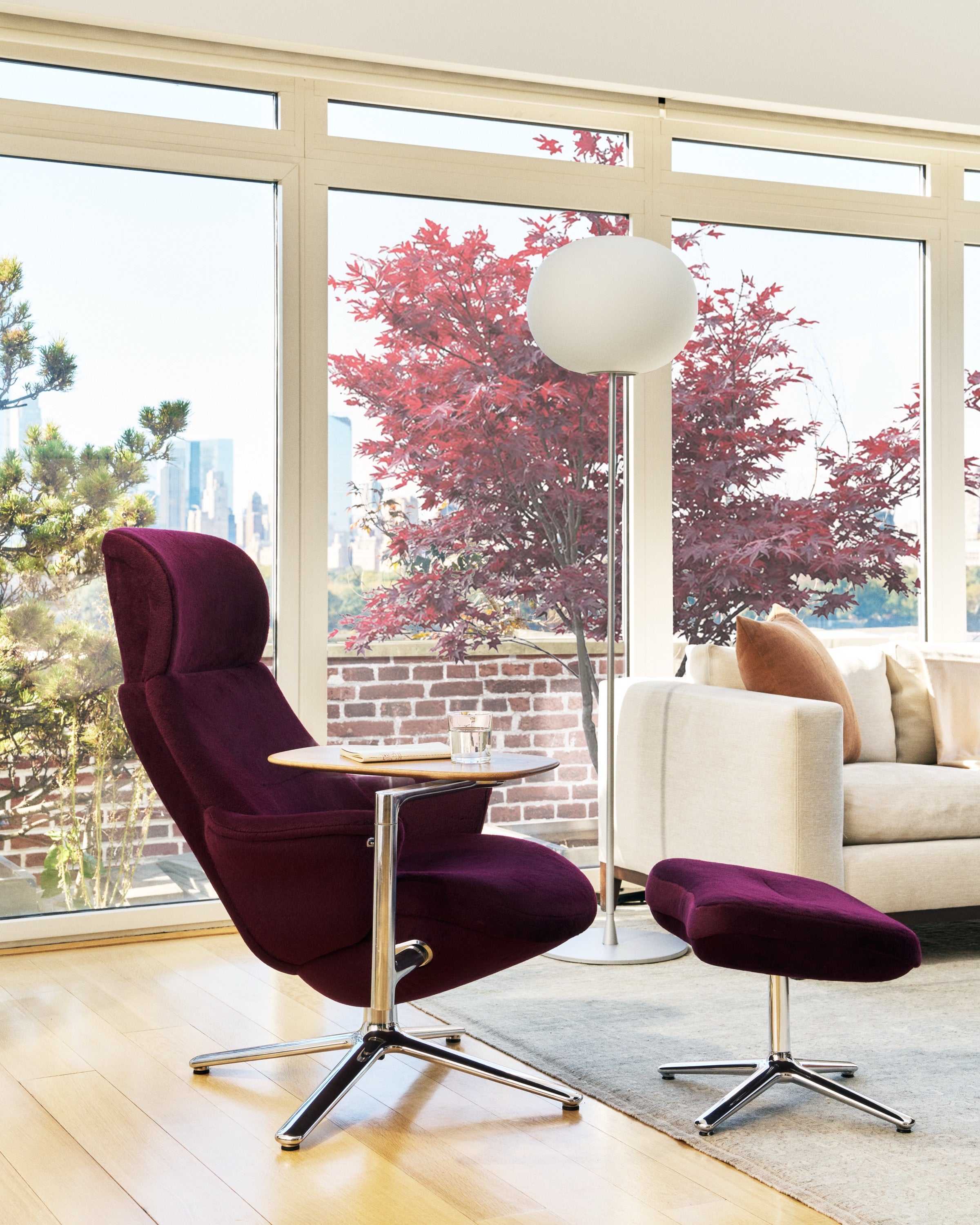 Wine Humanscale Diffrient Lounge chair with matching ottoman and side table in a modern living room with an urban skyline view