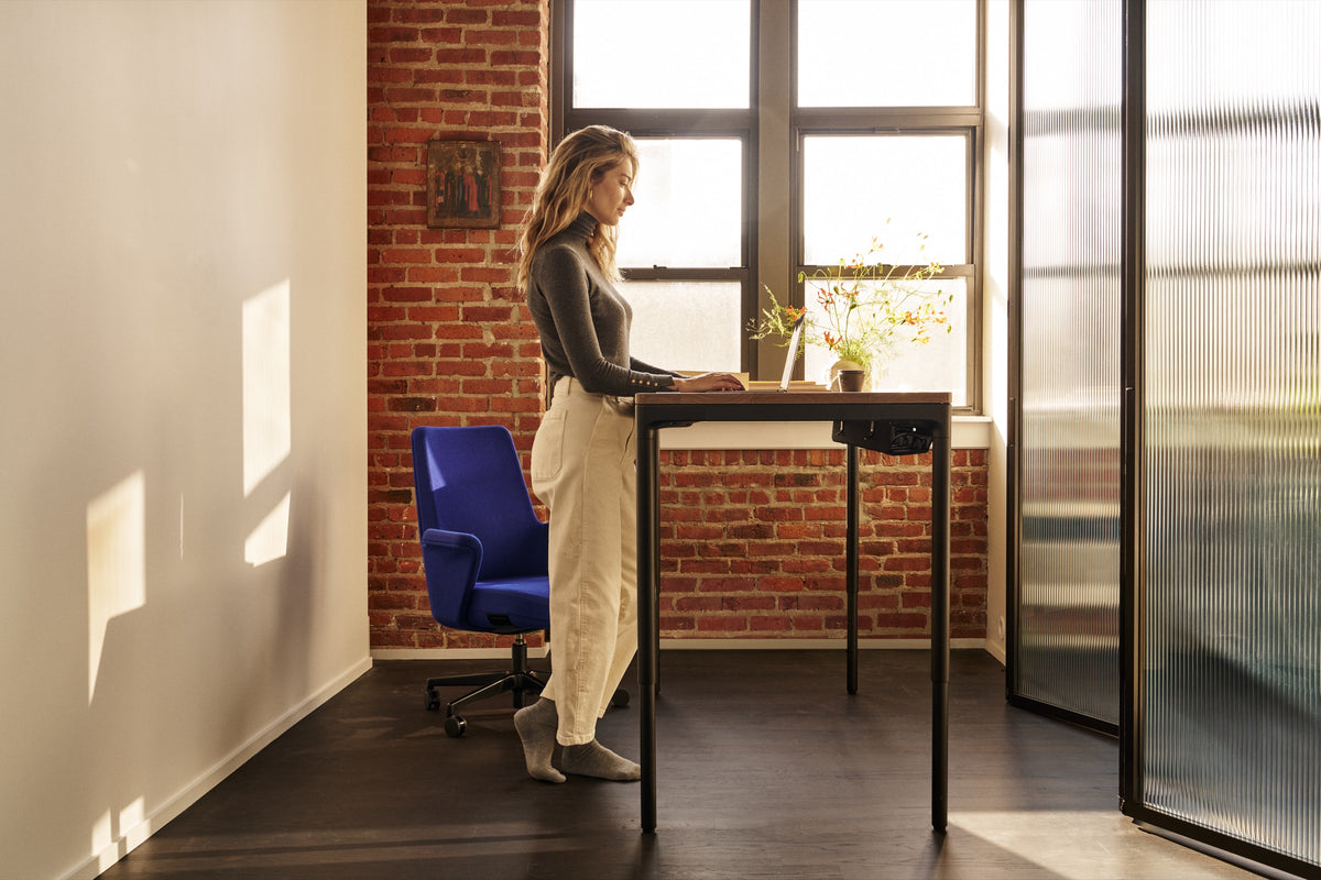 A person standing and working at a Humanscale eFloat Quattro desk, using the digital programmable switch to adjust the height for a healthy standing position