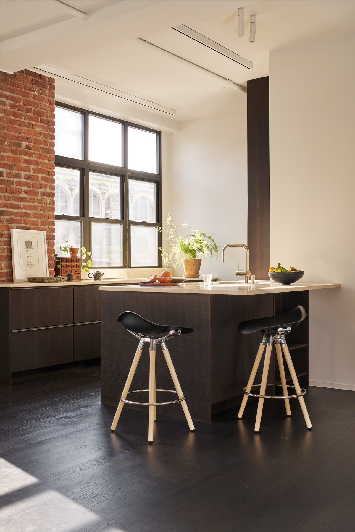 Two bar height Humanscale Sedeo stools with solid maple wood legs, black frames, and black seats at a modern kitchen island counter