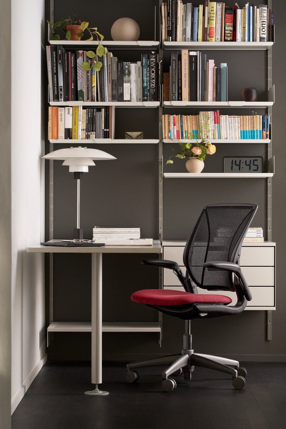 A black Humanscale Diffrient World office chair with Black Monofilament Stripe mesh back, a dark red upholstered seat, and all-black frame and base in a modern home office corner setup
