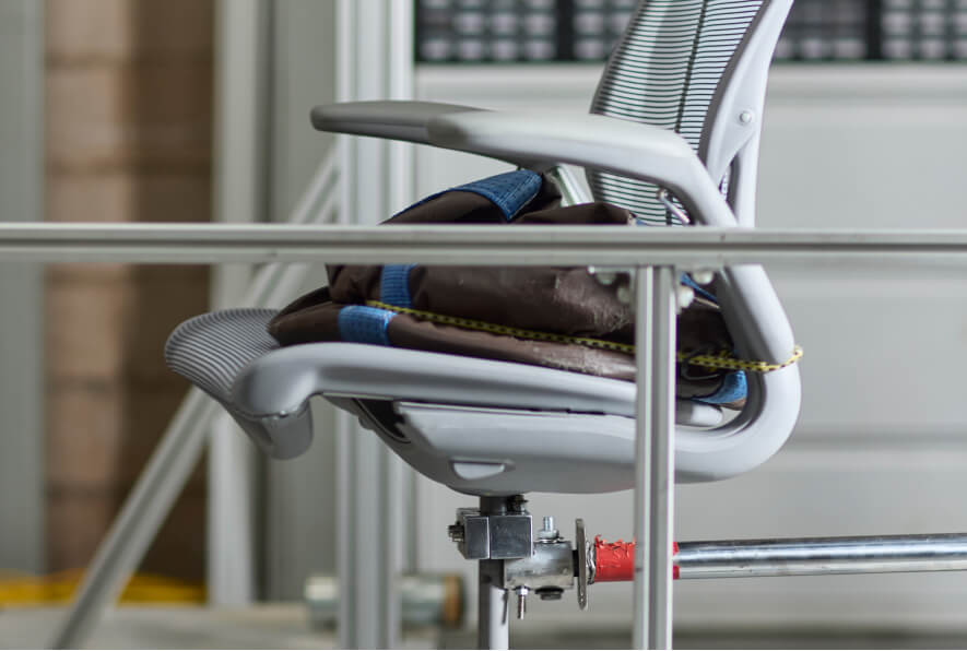 Side view of a white Humanscale Diffrient Smart chair made with 2lbs of ocean plastic, undergoing a certified 400lbs load and durability test in a laboratory setting