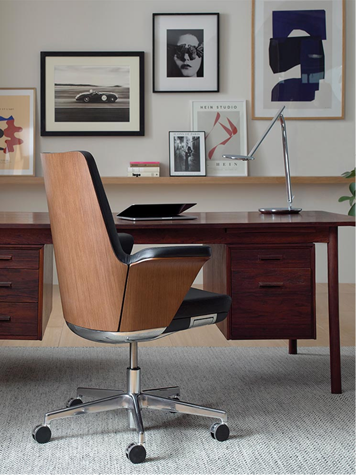 A rear diagonal view of a Humanscale Summa executive chair featuring a handcrafted ebony wood back, semiline black leather upholstery, and a polished aluminum base in a professional wood-paneled office