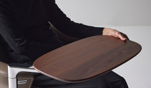 A close-up view of a person adjusting the smooth wood side table attached to the armrest of a Humanscale Diffrient Lounge chair