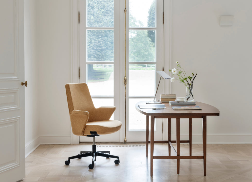 Tan upholstered Humanscale Summa executive conference chair with a black base in a warm modern home office with wooden desk and natural light