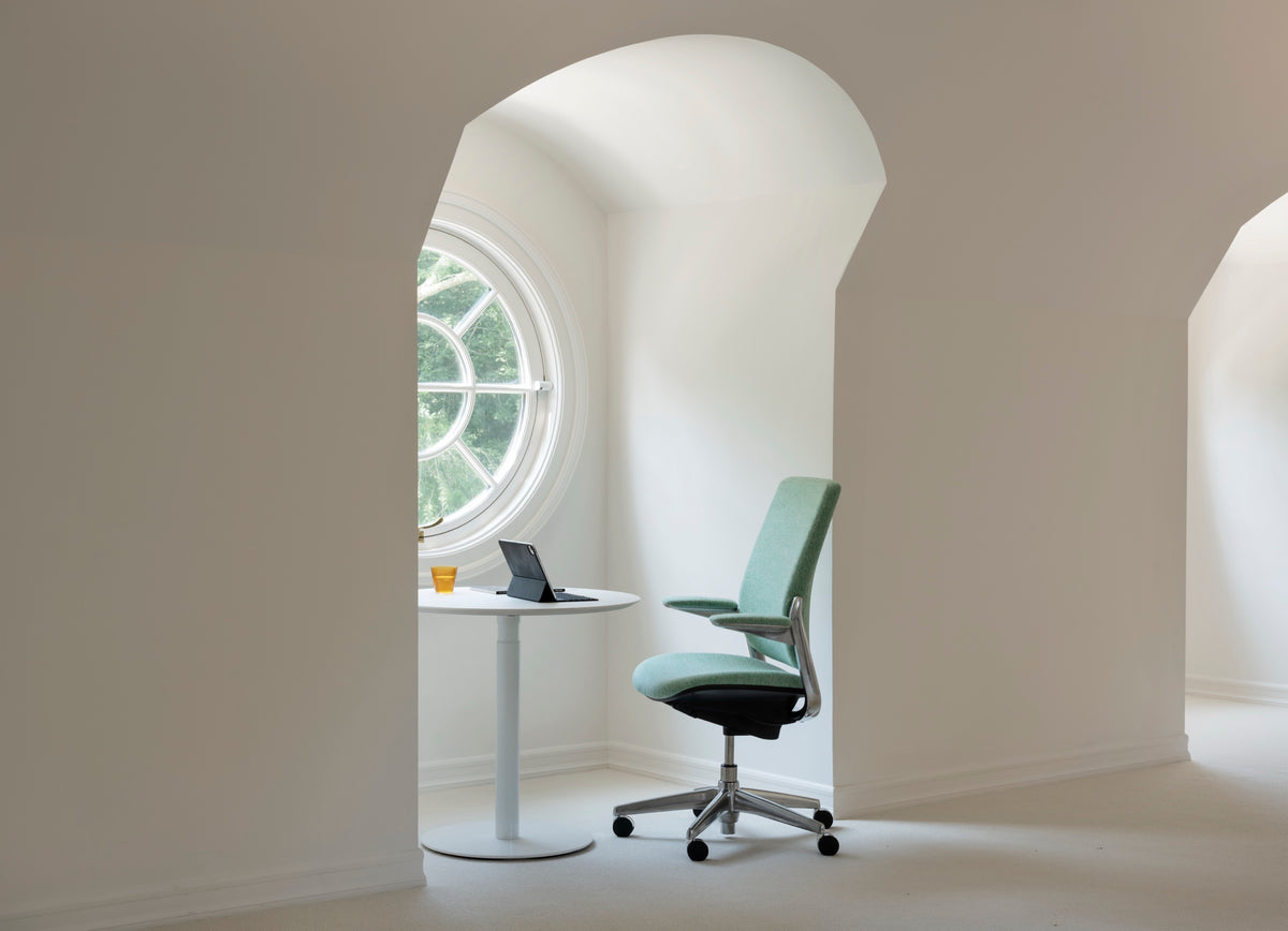 Diagonal front view of a Mint green Humanscale Smart Conference chair in chrome-free leather with a polished base next to a round table