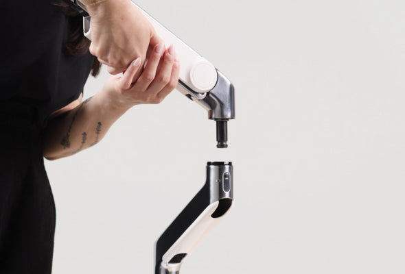 A person assembling a white and black adjustable arm mechanism for a Humanscale monitor arm, highlighting the precise industrial engineering and component quality