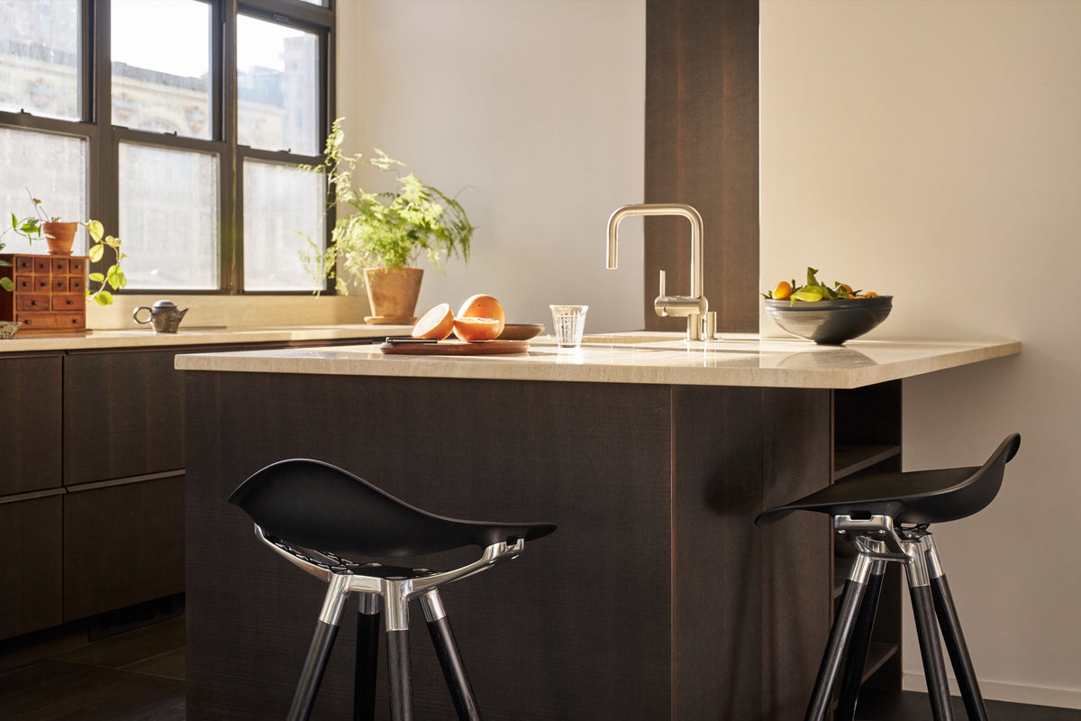 Two Humanscale Sedeo stools at a kitchen island, featuring bar-height Ebony Oak wood legs and polished aluminum frames with black seats, shown in side and back views