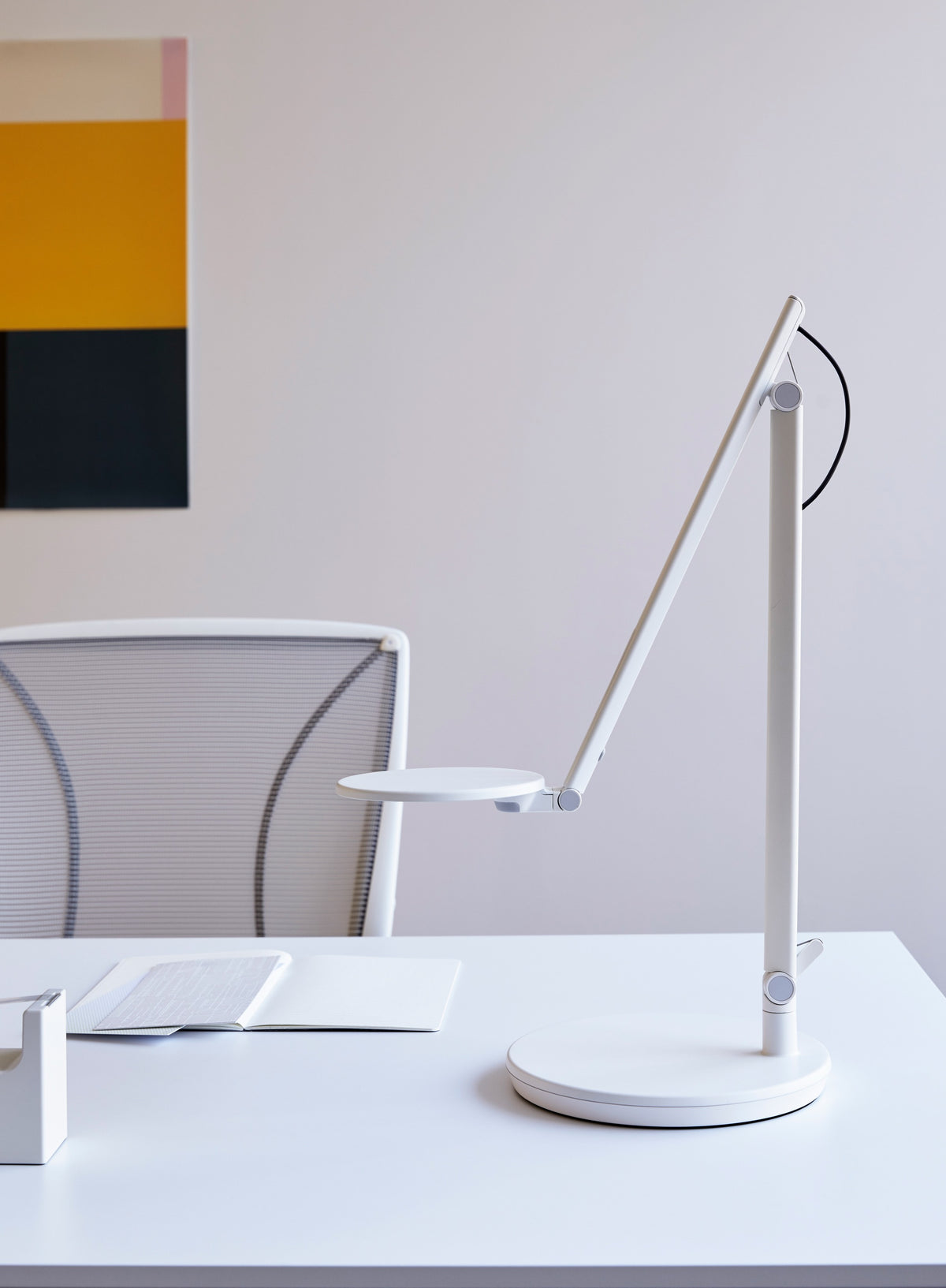 Side view of an Arctic White Humanscale Nova LED task lamp with an adjustable arm and circular light head on a clean white desk