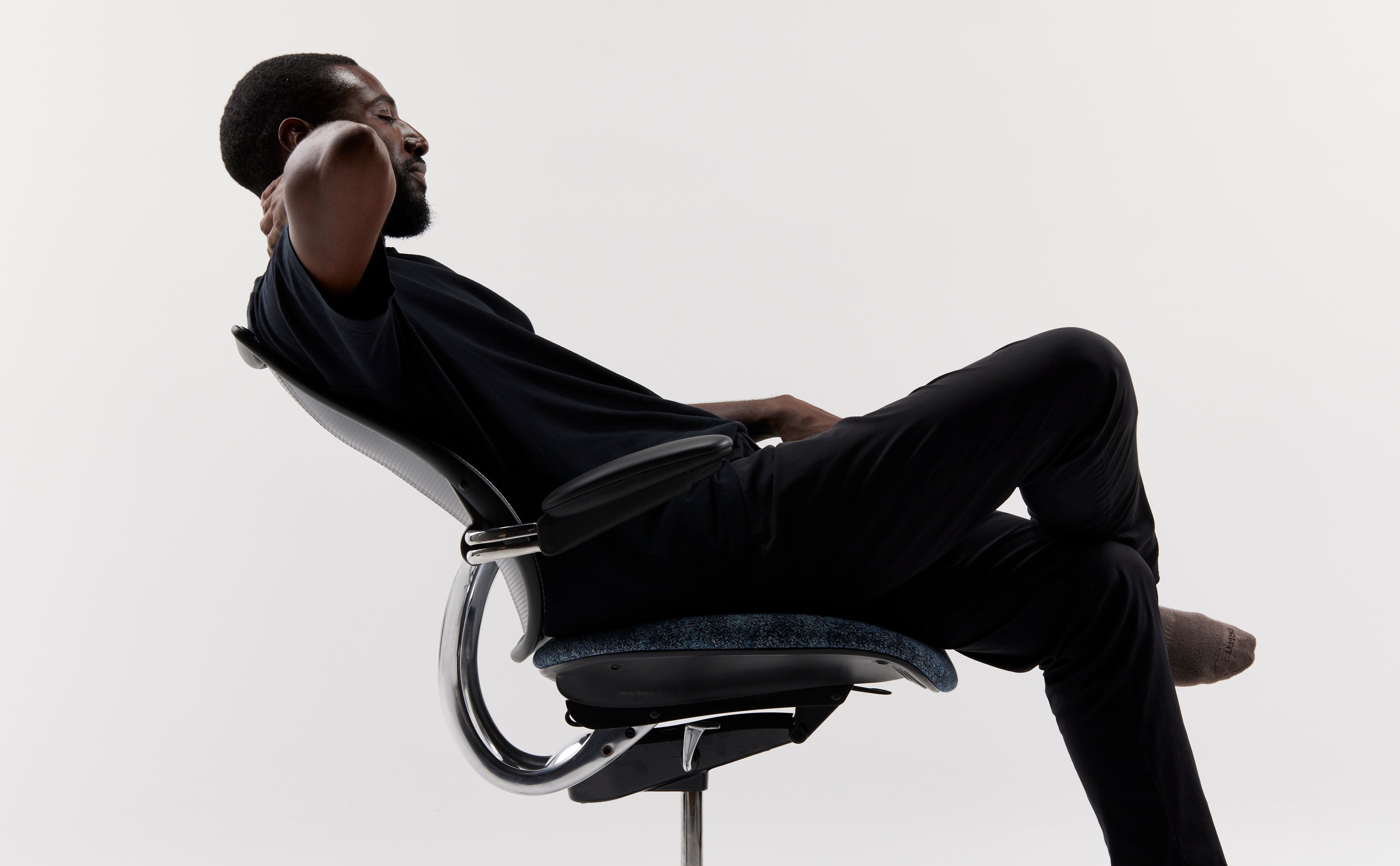 Man reclining in a Humanscale Liberty Ocean chair with pinstripe black mesh, a blue Vanir textile seat, and a polished aluminum frame with black trim