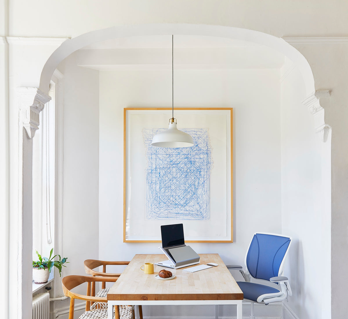 Blue and white Humanscale Diffrient World chair with pinstripe mesh and an L6 laptop holder on a wooden dining table in a modern home office