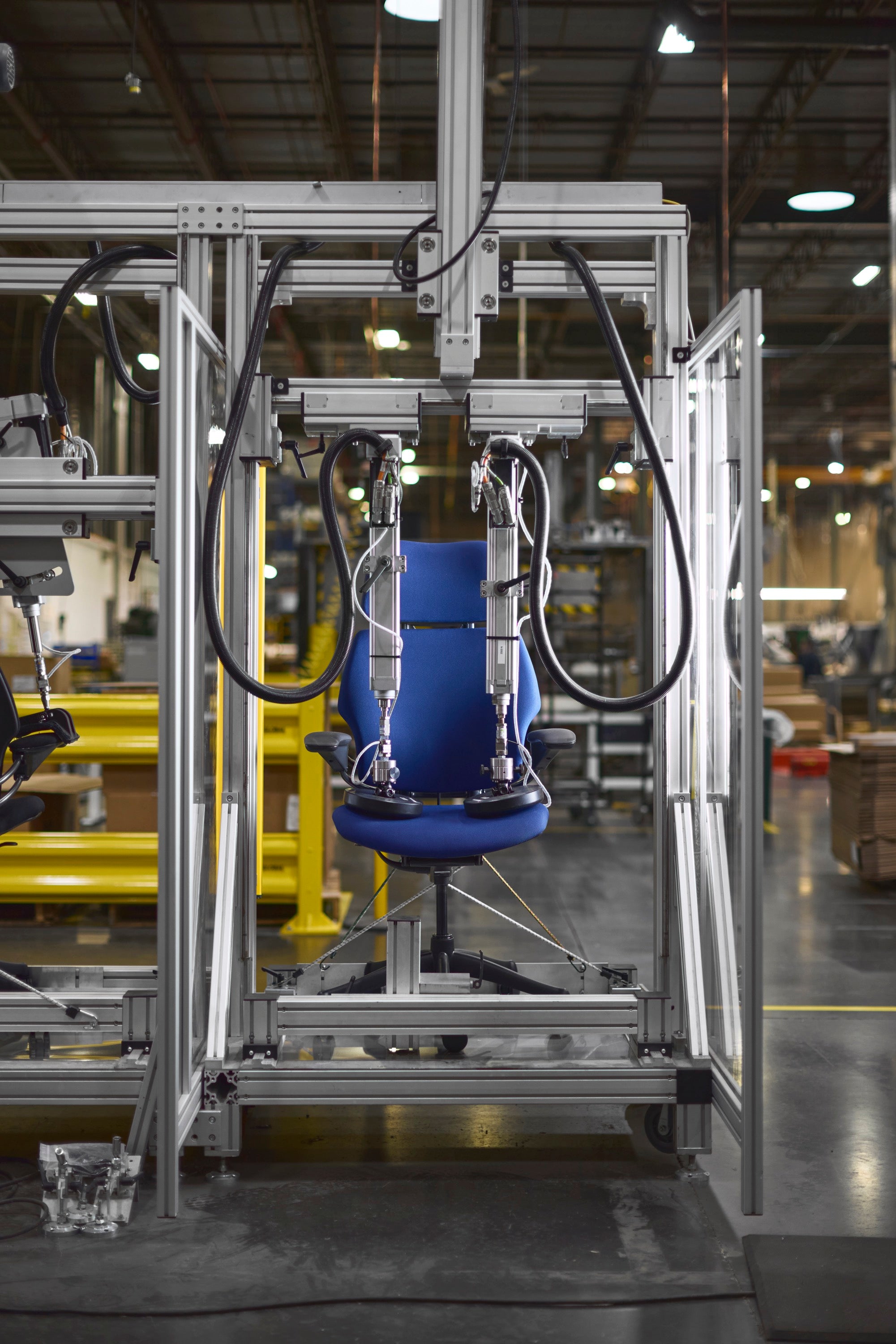 Azure blue Humanscale Freedom Ocean headrest chair with a black frame undergoing rigorous mechanical durability and pressure testing in a factory rig