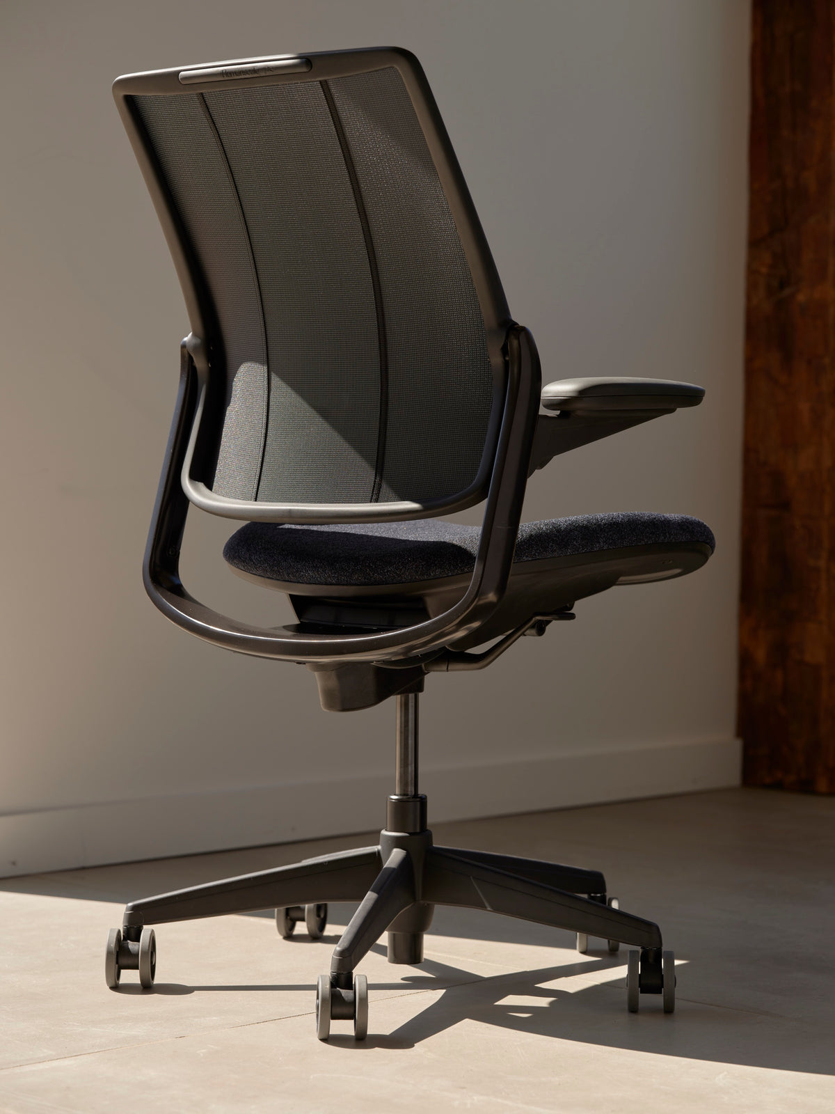 Rear angle view of a Humanscale Diffrient Smart chair showing the silver frame, silver trim, and black tri-paneled mesh with a dark brown seat