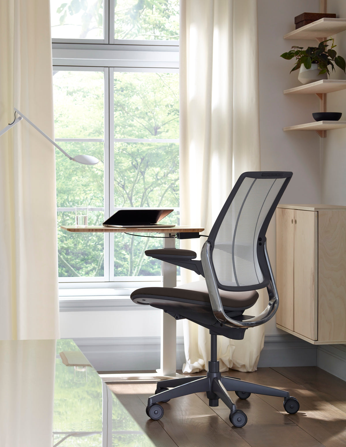 Back view of a Humanscale Diffrient Smart chair with black tri-paneled mesh and silver frame at an adjustable standing desk in a bright home office