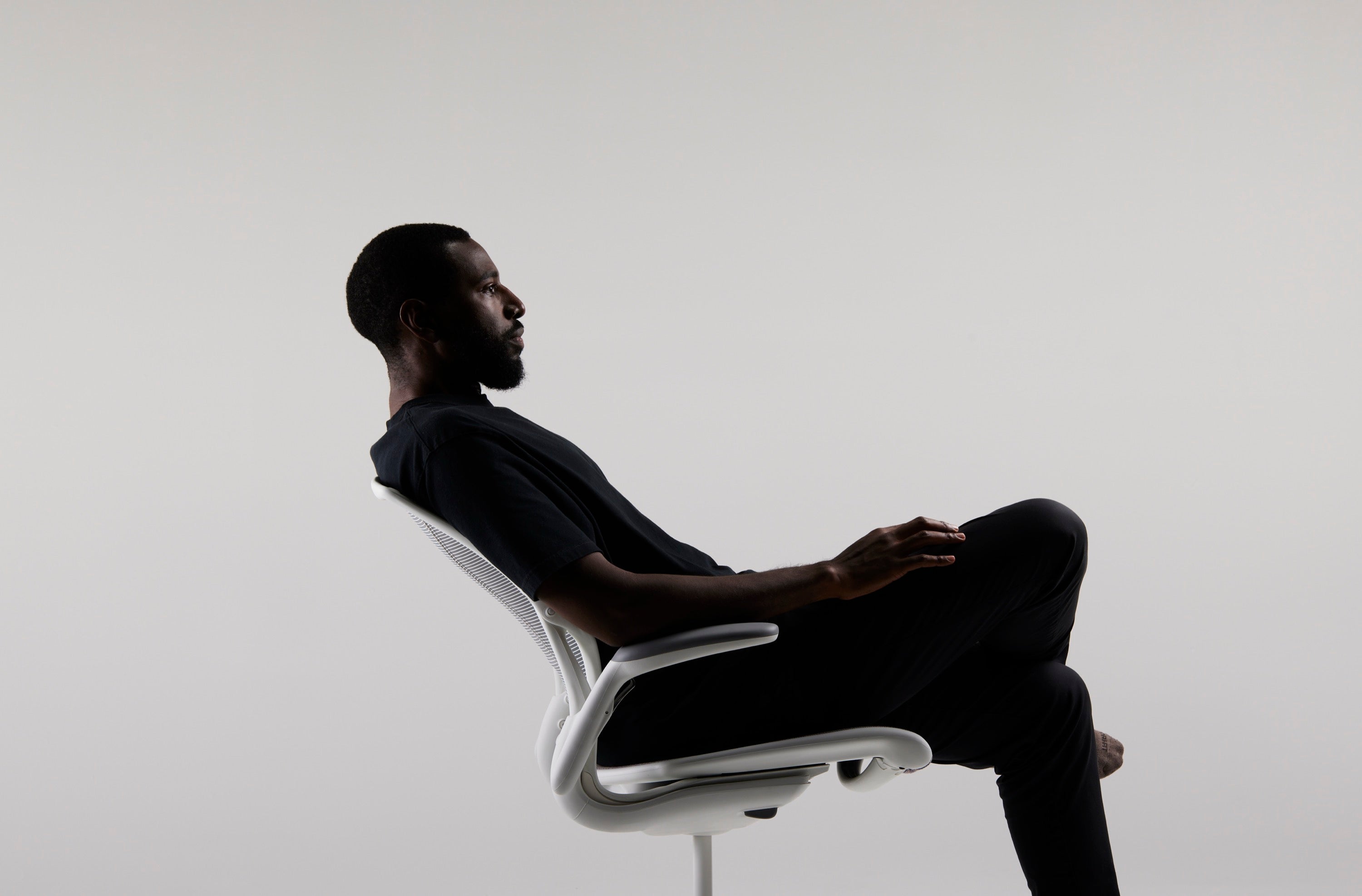 Man leaning back in a white Humanscale Diffrient World task chair featuring pinstripe white mesh on the back and seat with a white frame