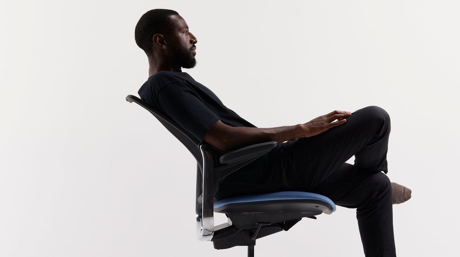 Profile view of a man reclining in a Humanscale Diffrient Smart Ocean task chair showing how the arms move with the backrest, featuring a blue textile seat and black frame