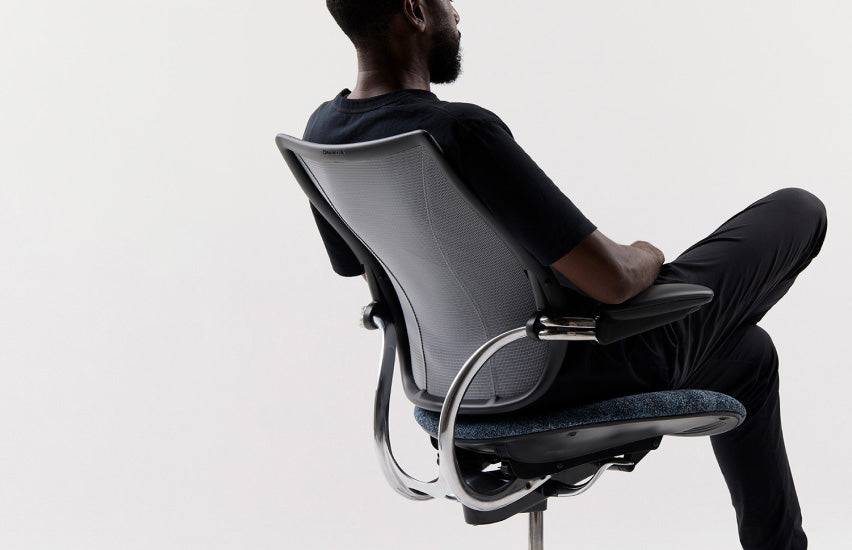 Rear diagonal view of a man seated in a Humanscale Liberty Ocean task chair with pinstripe black mesh, polished aluminum frame, and black trim