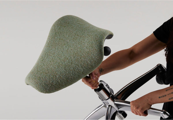 Person holding a Humanscale Freedom saddle stool in light green fabric.