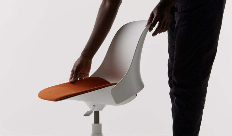 Side view of a person adjusting the burnt orange seat of a Humanscale Trea white chair